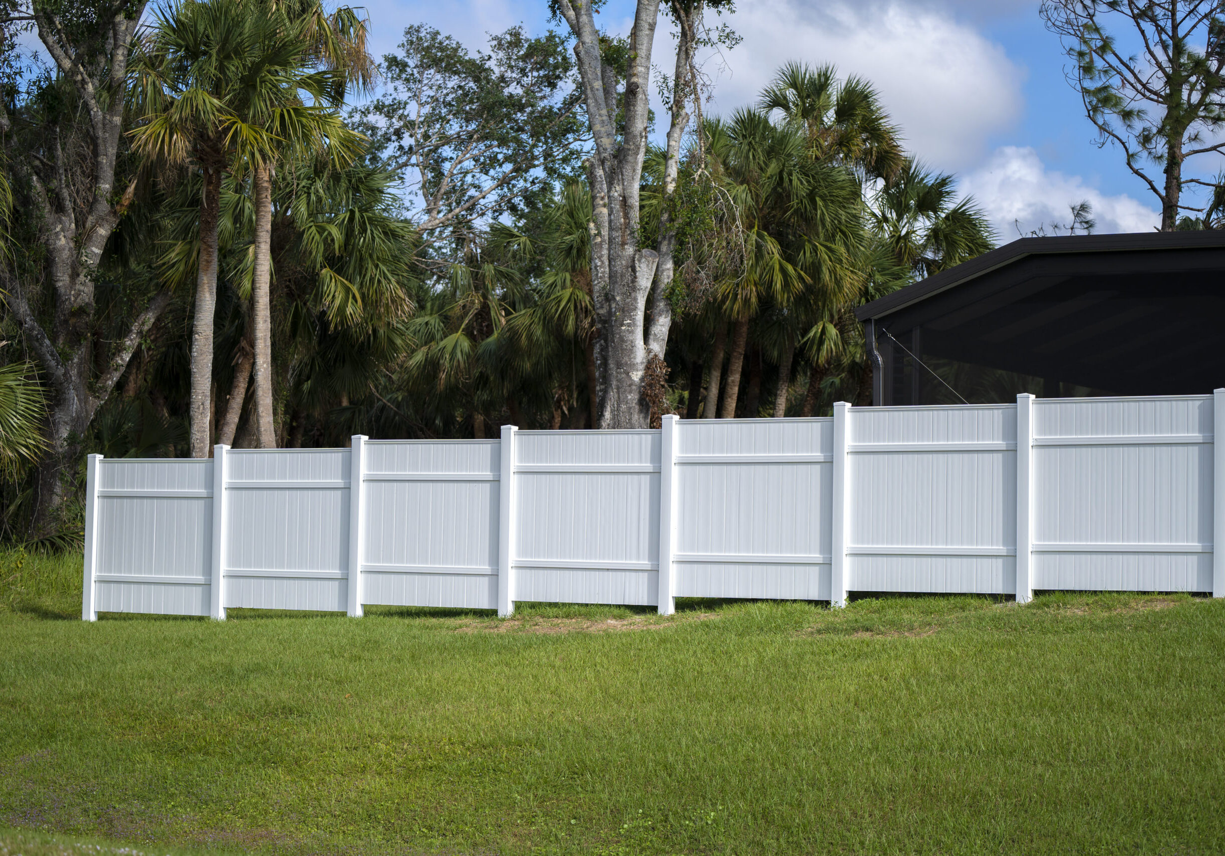 White vinyl picket fence on green lawn surrounding property grounds for backyard protection and privacy.